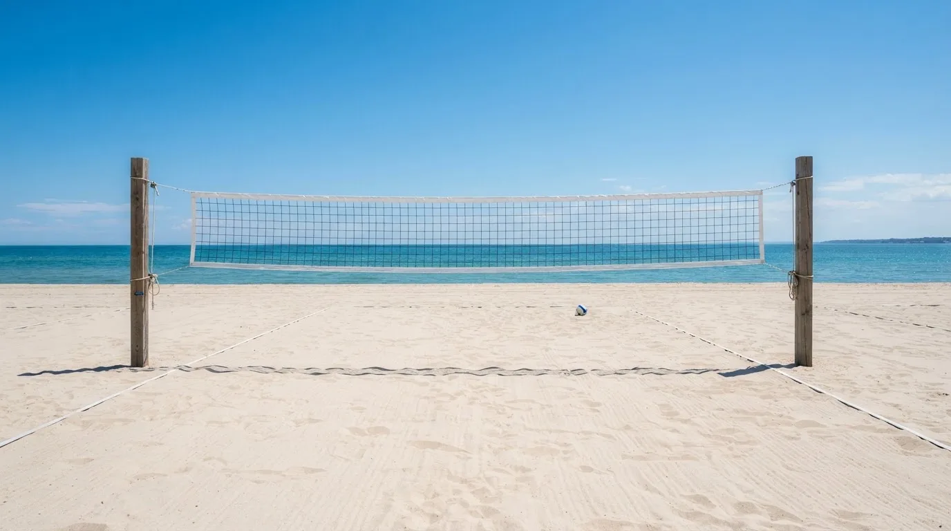 Siatka do siatkówki rozpięta nad piaszczystym boiskiem plażowym pod czystym niebem.