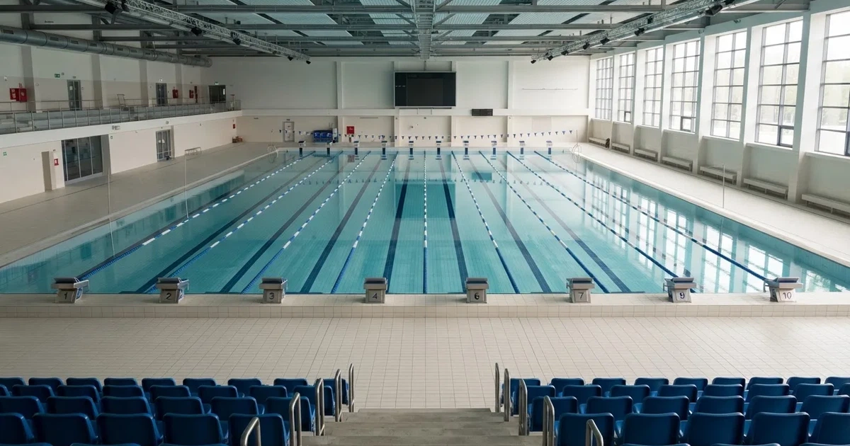 Pusty basen olimpijski z równymi torami i spokojną taflą wody, widok z trybun w jasnym świetle.
